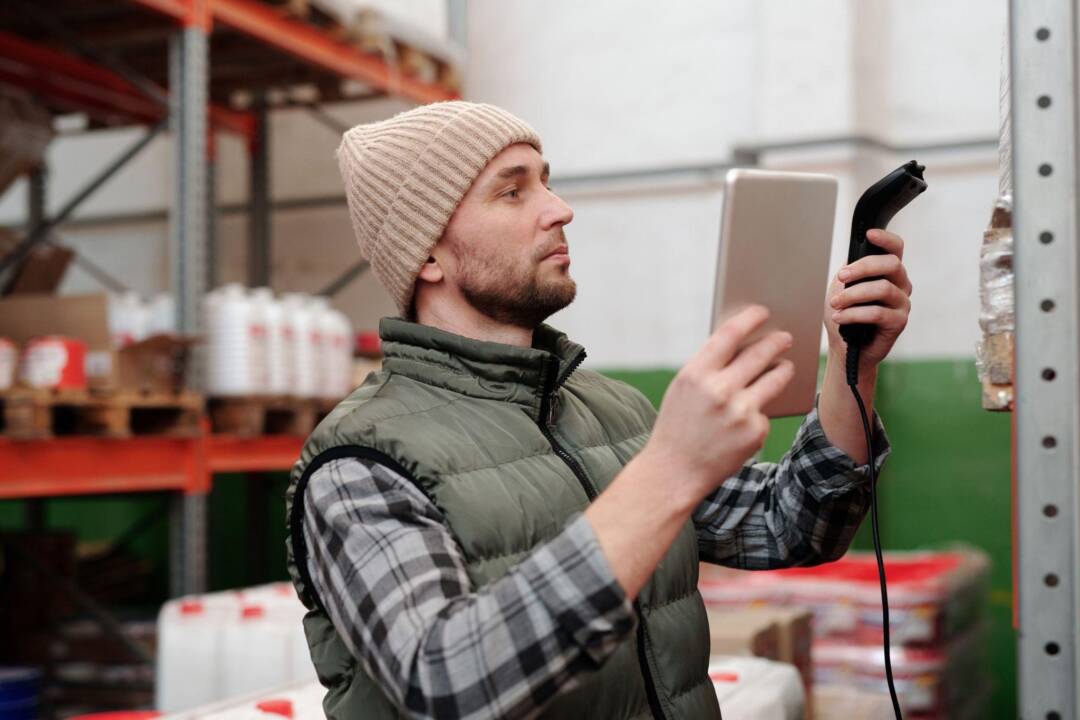 Warehouse worker scanning inventory with a tablet, reflecting warehousing tech standards.